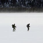 Two bison researchers wearing packs ski across a flat area