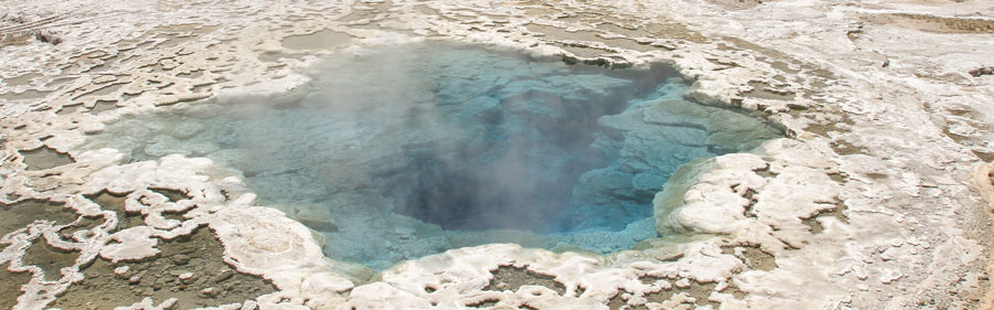 A blue hot spring pool steams, surrounded by a scaly white landscape.