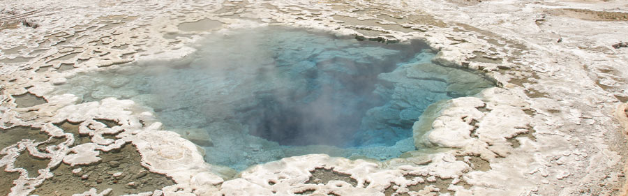 Artemesia geyser A blue hot spring pool steams, surrounded by a scaly white landscape.