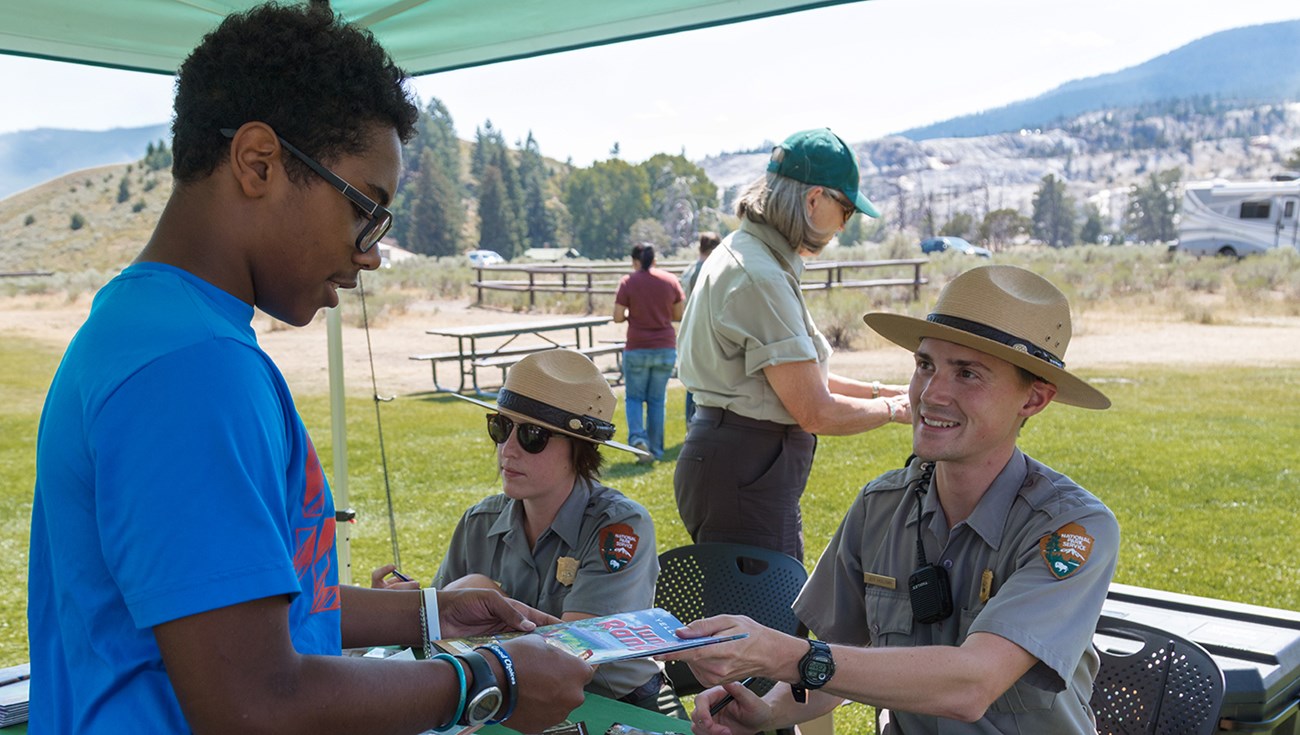 A child is handed a booklet by a park ranger while another ranger looks on.