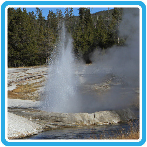 An eruption of water and steam rises from a crater on the bank of a small river.