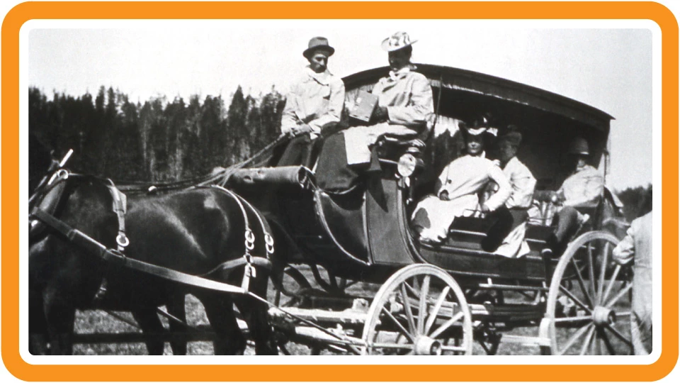 Visitors in a horse-drawn stagecoach A man and woman sit at the front of a stagecoach, holding the reins, while three other passengers look out from the coach.