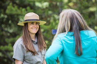 A uniformed person talking to another person with camera.
