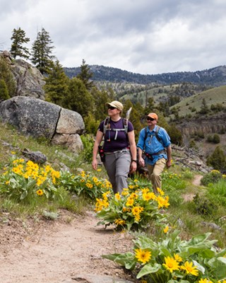 A man and woman hiking along a trail through yellow flowers