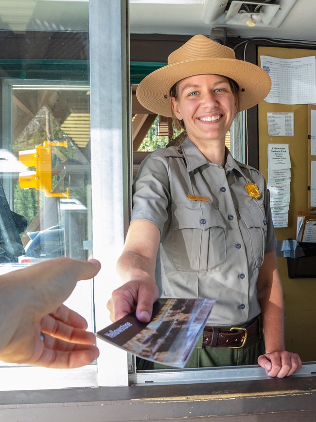 a person in a park ranger uniform at an entrance station handing out a park map