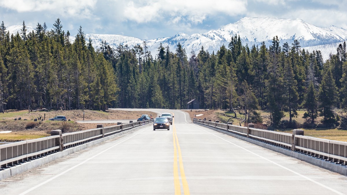 cars driving on a bridge with snowy mountains in the distance