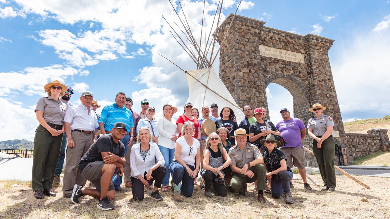 a group of people standing next to a large, white teepee and stone archway