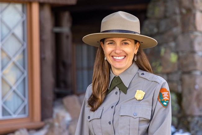 A woman wearing a National Park Service uniform and flat hat and smiling at the camera