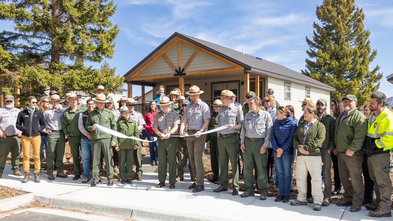 a group of people cutting a large, white ribbon in front of brand-new housing units