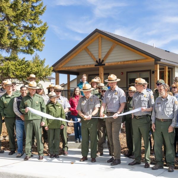 a large group of people cutting a white ribbon in front of new housing