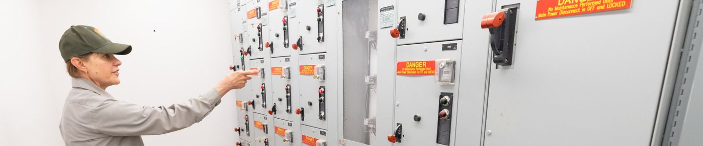 A park maintenance worker pointing at an array of buttons in a wastewater treatment plant