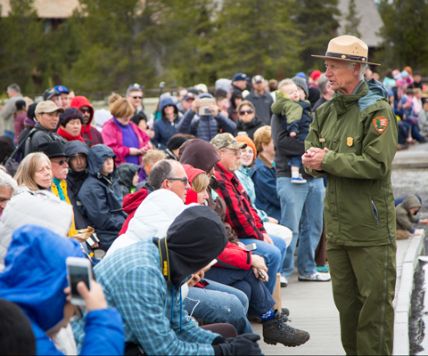 A male park ranger speaks to seated visitors on a boardwalk