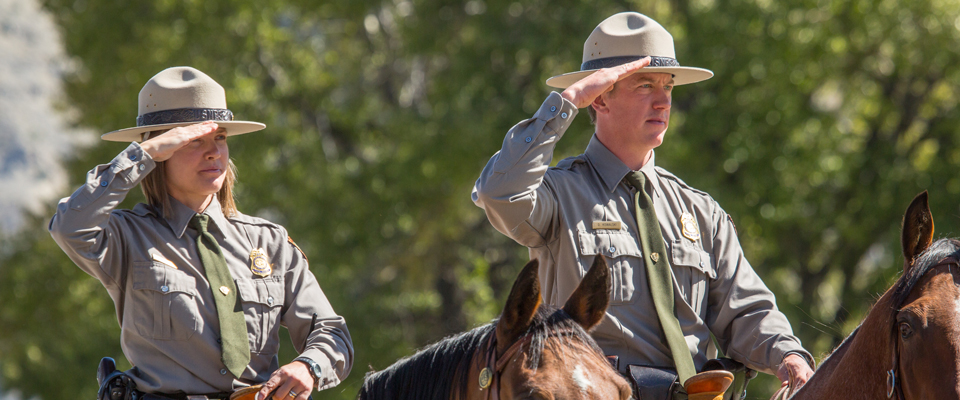 Two park rangers on horseback salute Two park rangers on horseback salute