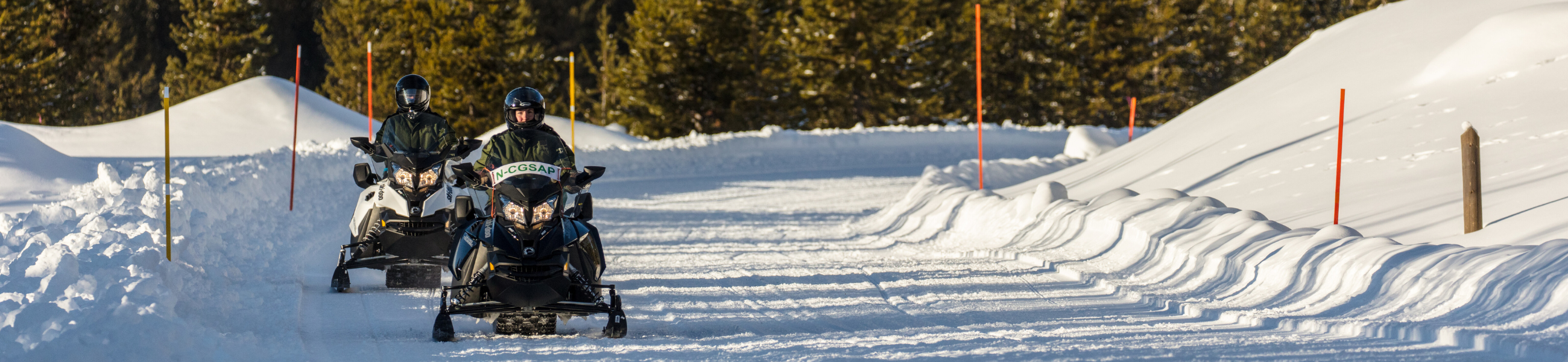 two people riding snowmobiles on a snowy road