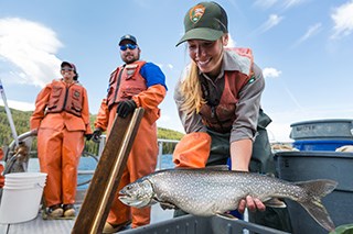 A person in a boat holding a lake trout