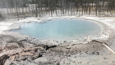 Murky waters of Cistern Spring surrounded by a gray, muddy landscape.