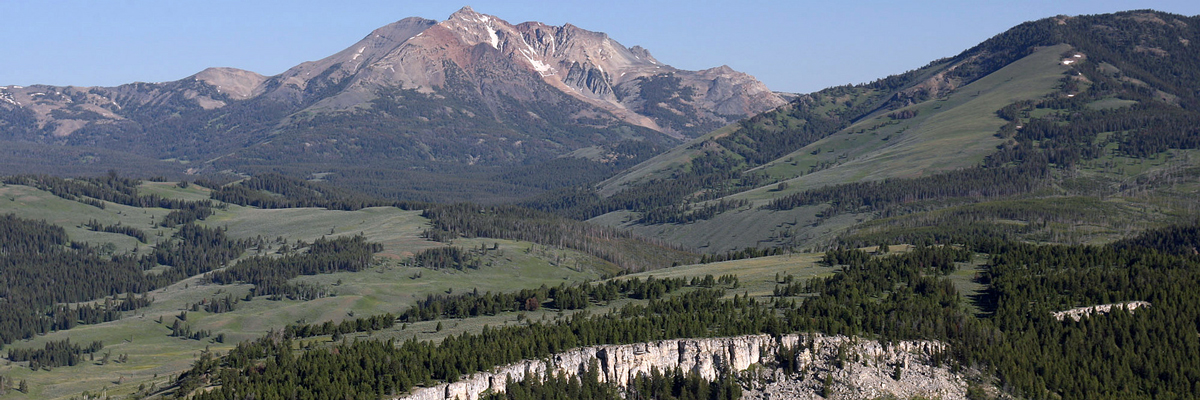 A mountain with sloped green hills and bare rock at the top of a hill in the foreground A mountain with sloped green hills and bare rock at the top of a hill in the foreground