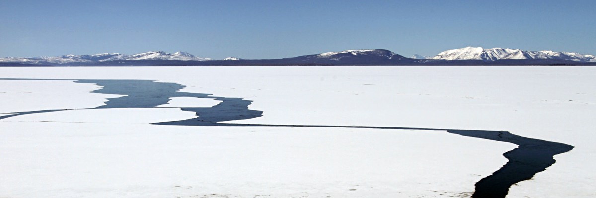 Distant snow-covered mountains and an ice-covered lake with large cracks
