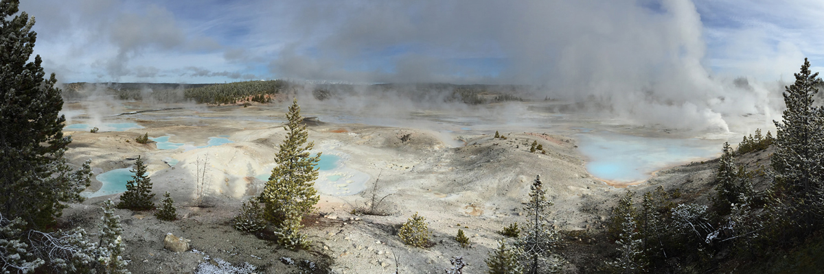 Steam rises from a wide geyser basin with light blue pools Steam rises from a wide geyser basin with light blue pools
