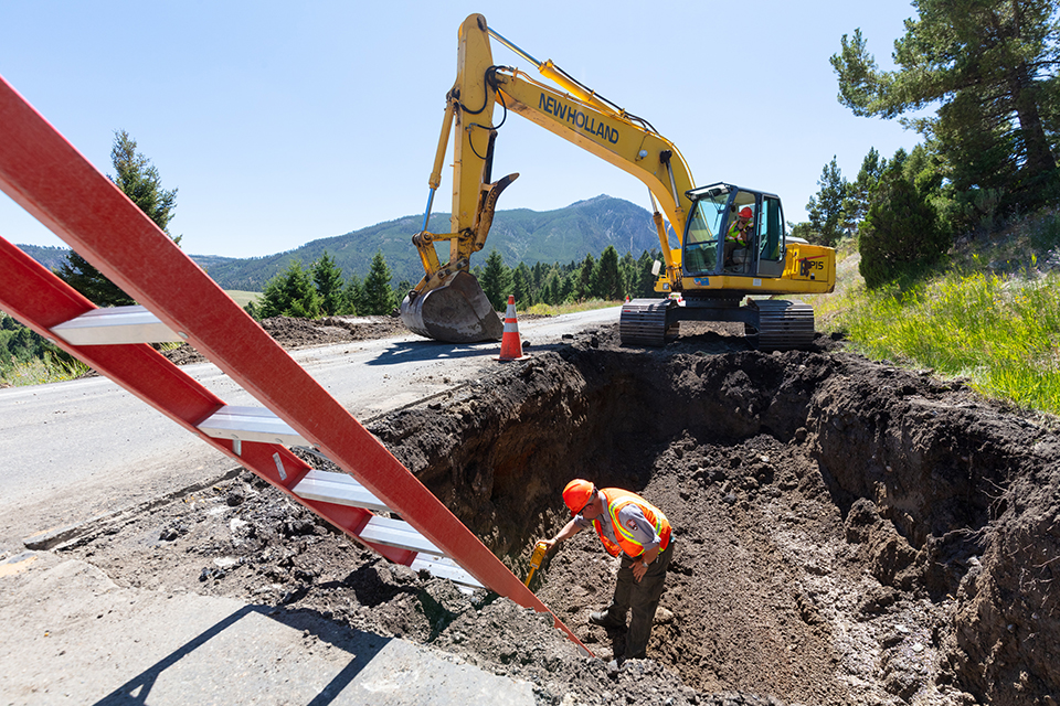 Employee using a wand to locate a water main in an excavated hole in the road