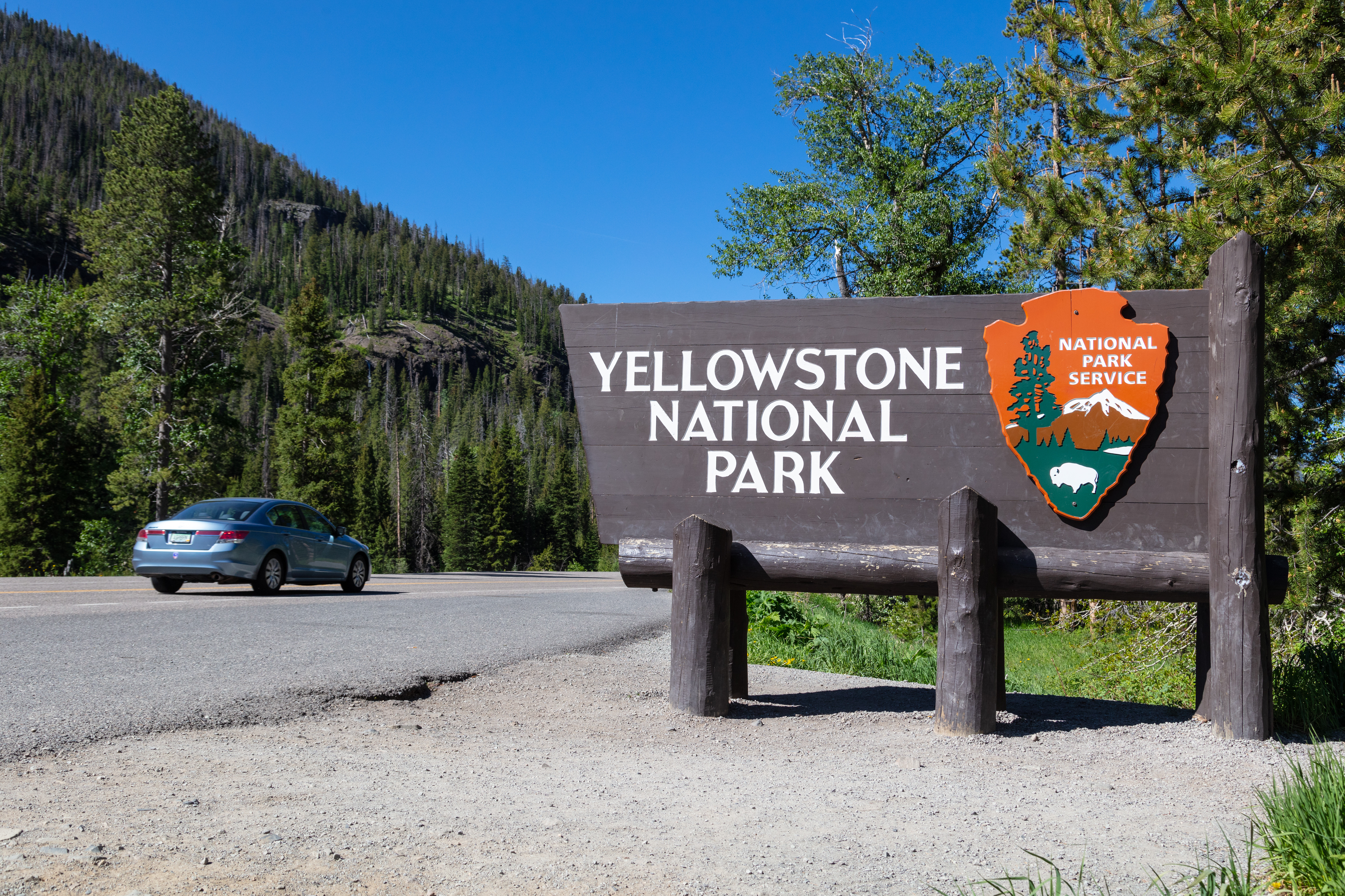 a large wooden sign next to a road with text: "Yellowstone National Park"