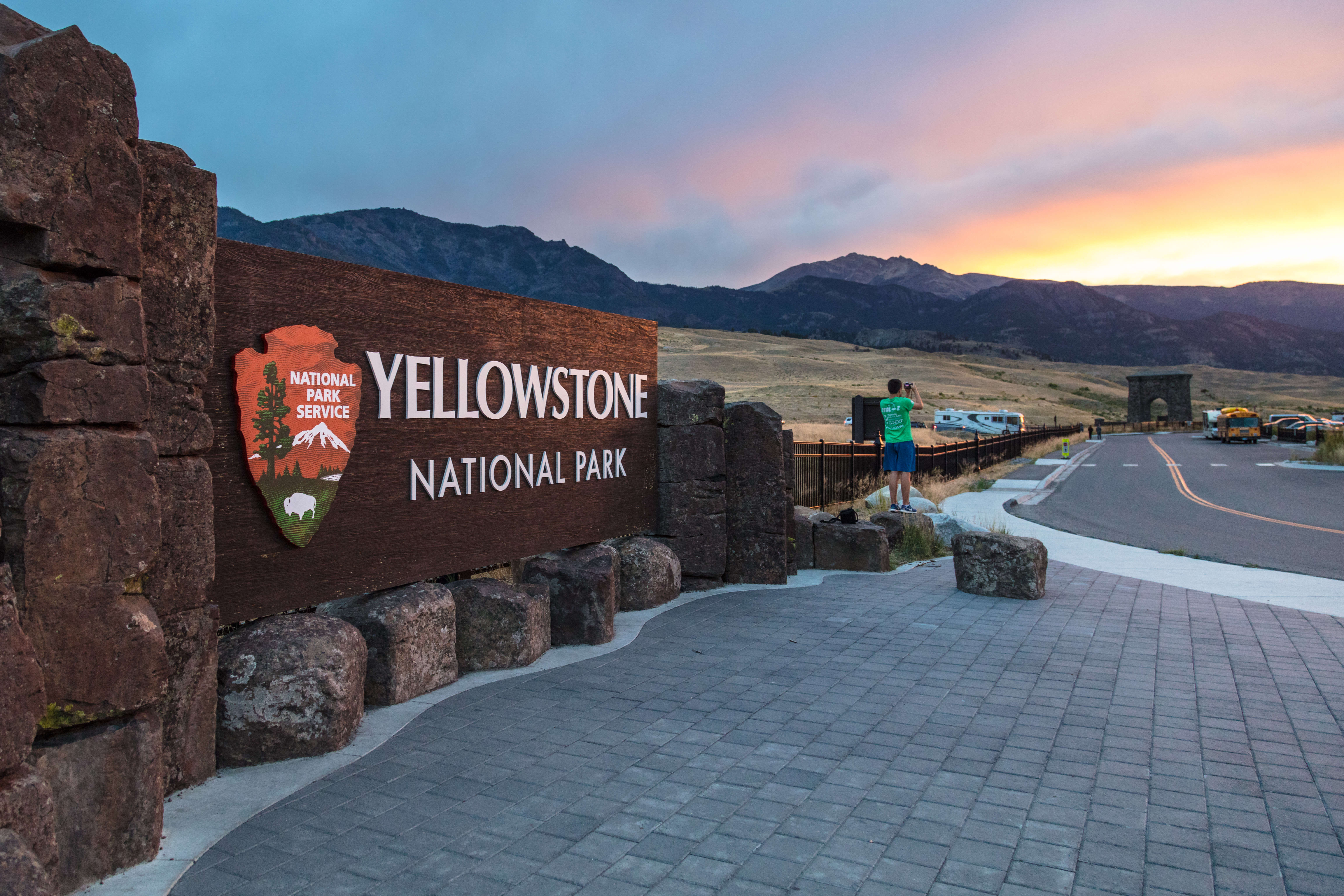 A large Yellowstone National Park sign in front of mountains at sunset