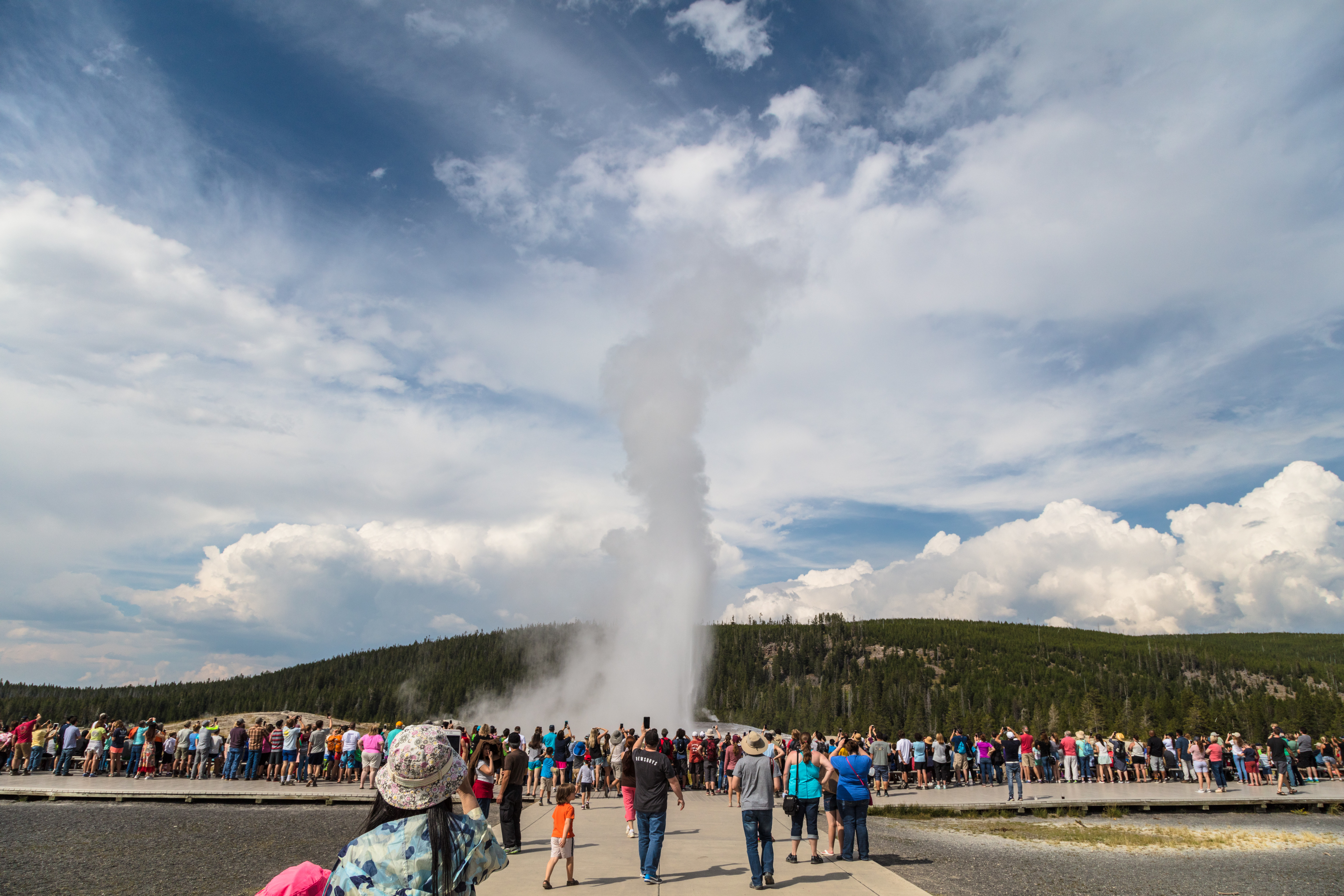 A crowd of people watching a geyser erupt