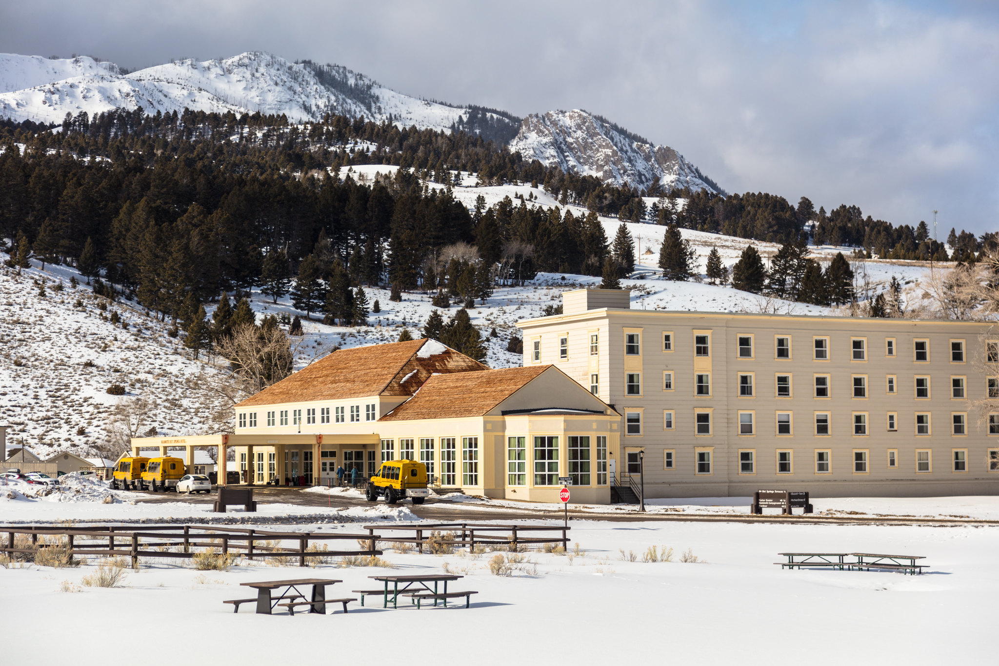 A large white hotel sits below mountains in the background. Snow covers the ground.