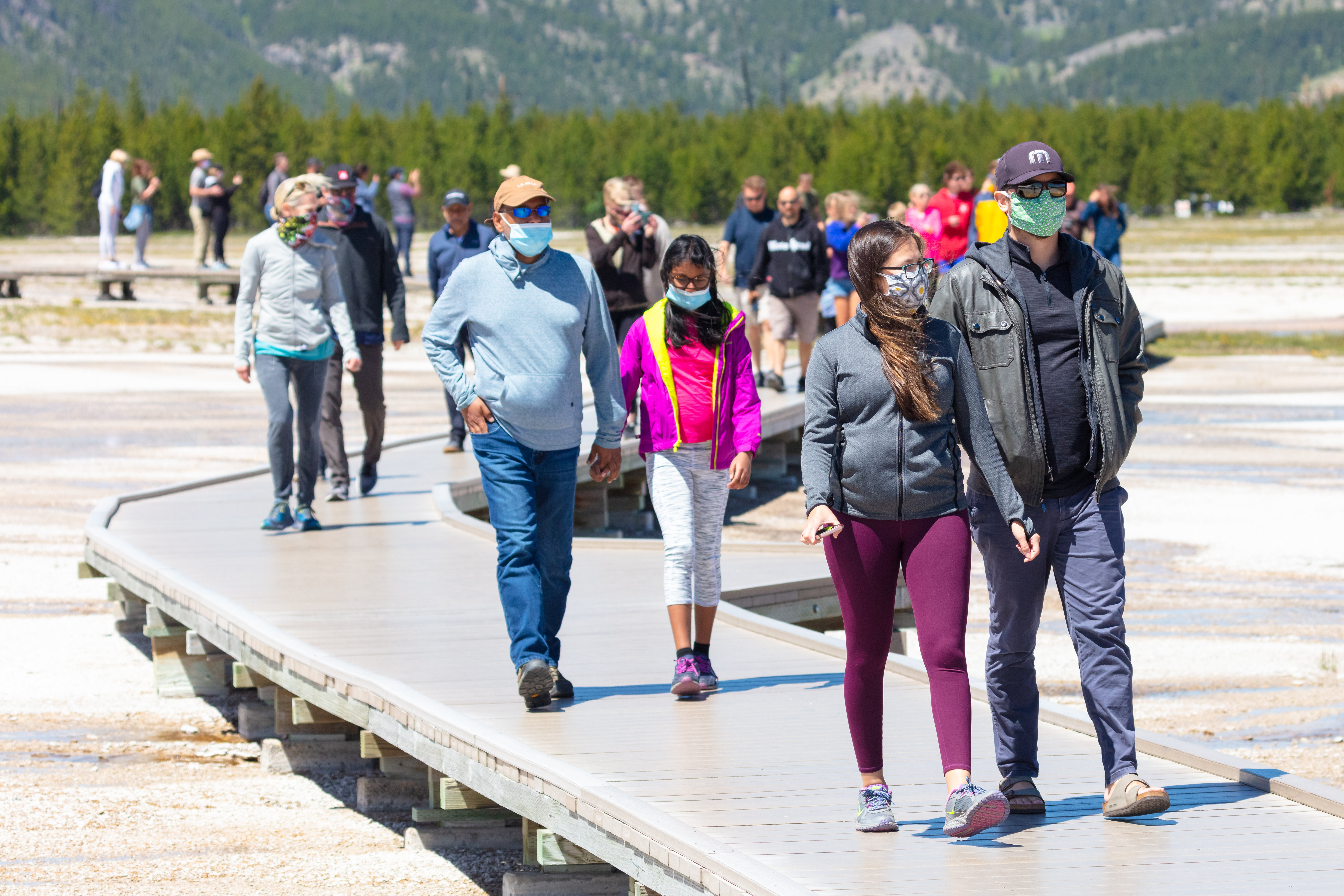 People, some wearing masks, walking on a boardwalk