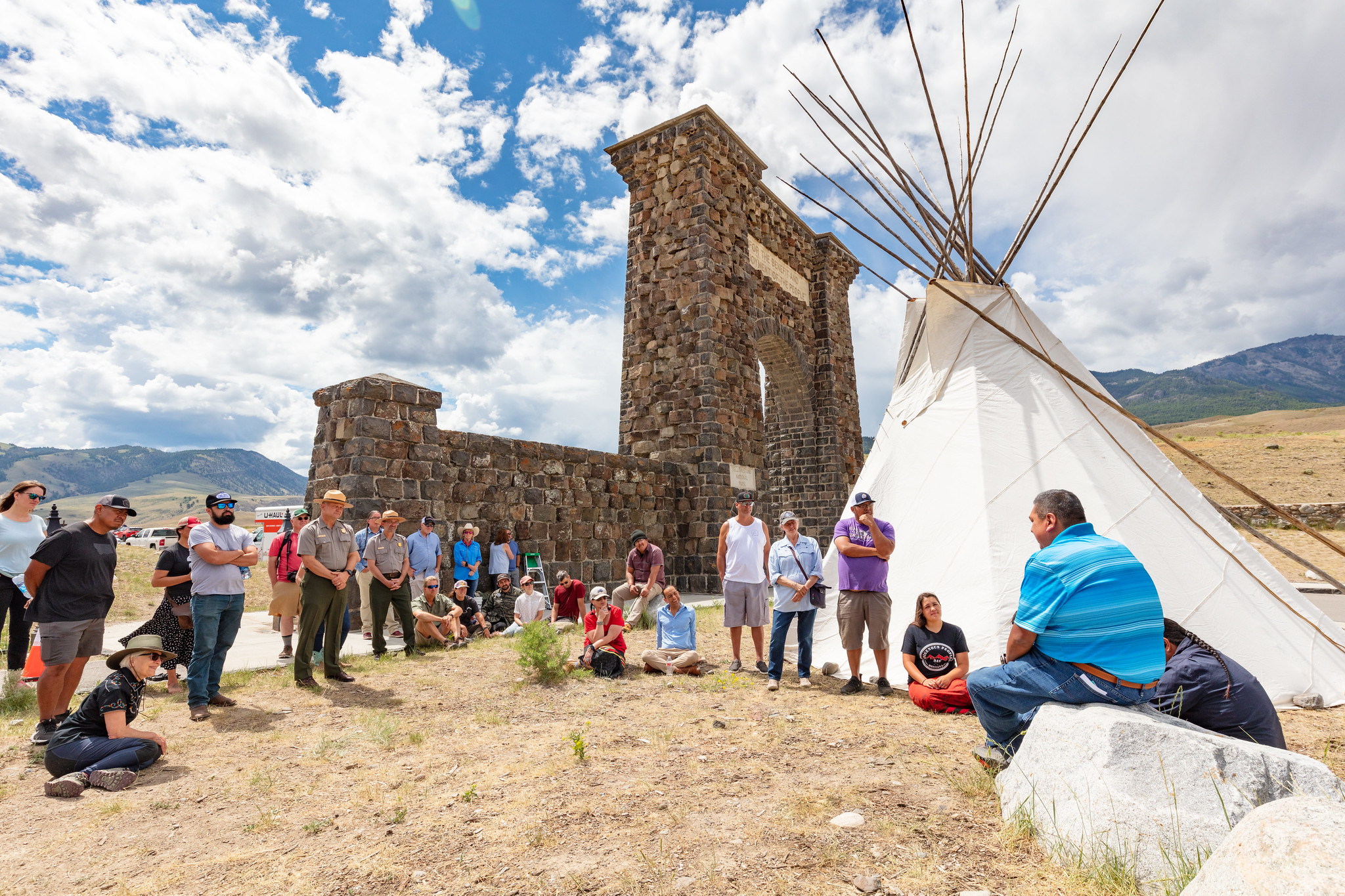 tribal members and park staff stand in front of tipi and Roosevelt Arch