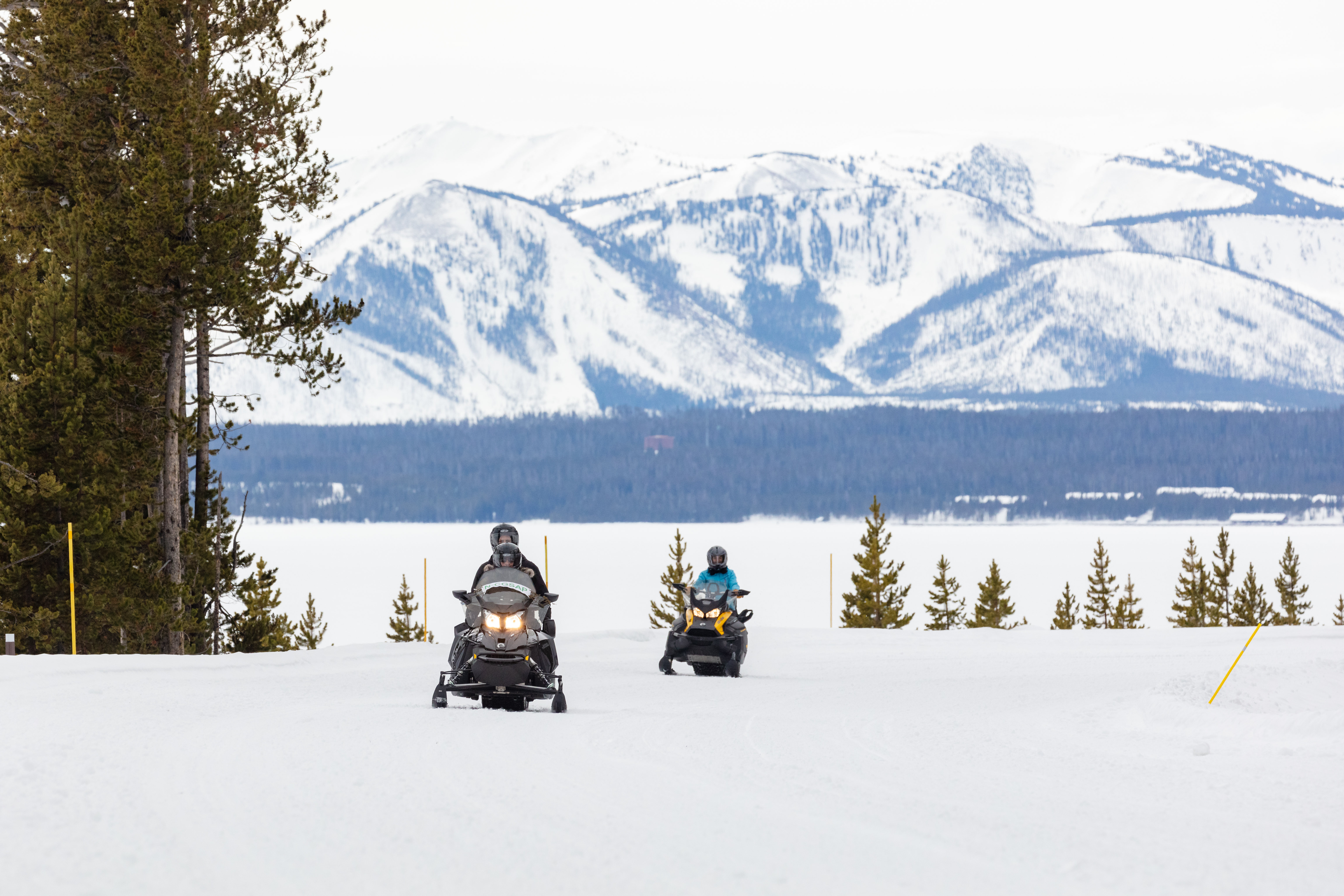 two snowmobilers driving through a wintry mountainous landscape