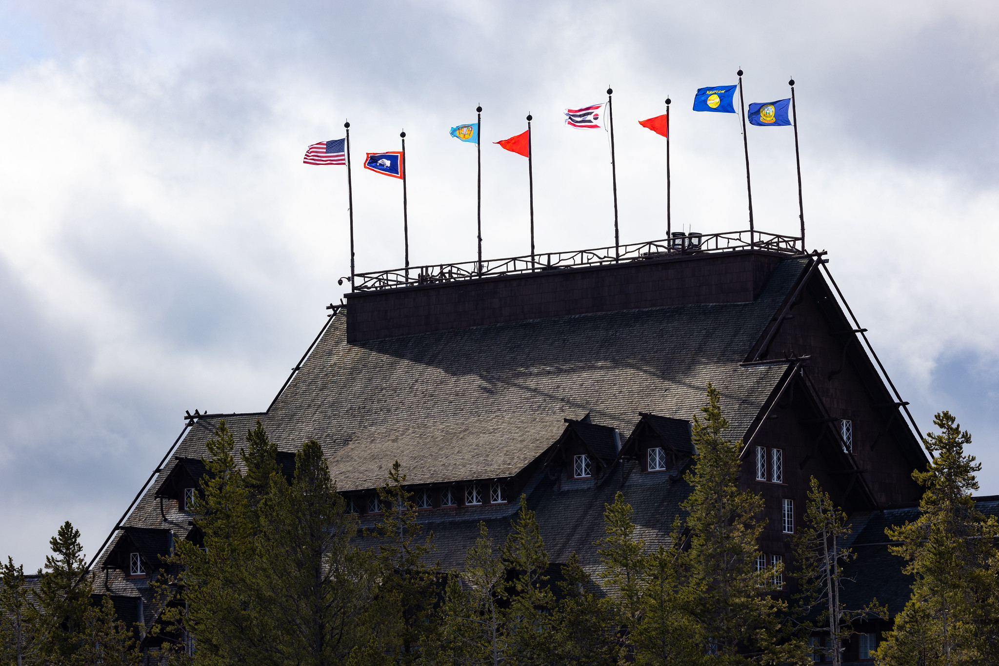 Yellowstone National Park Lodges 150 Years of Inspiration Event: Tribal, State, and US flags fly atop the Old Faithful Inn