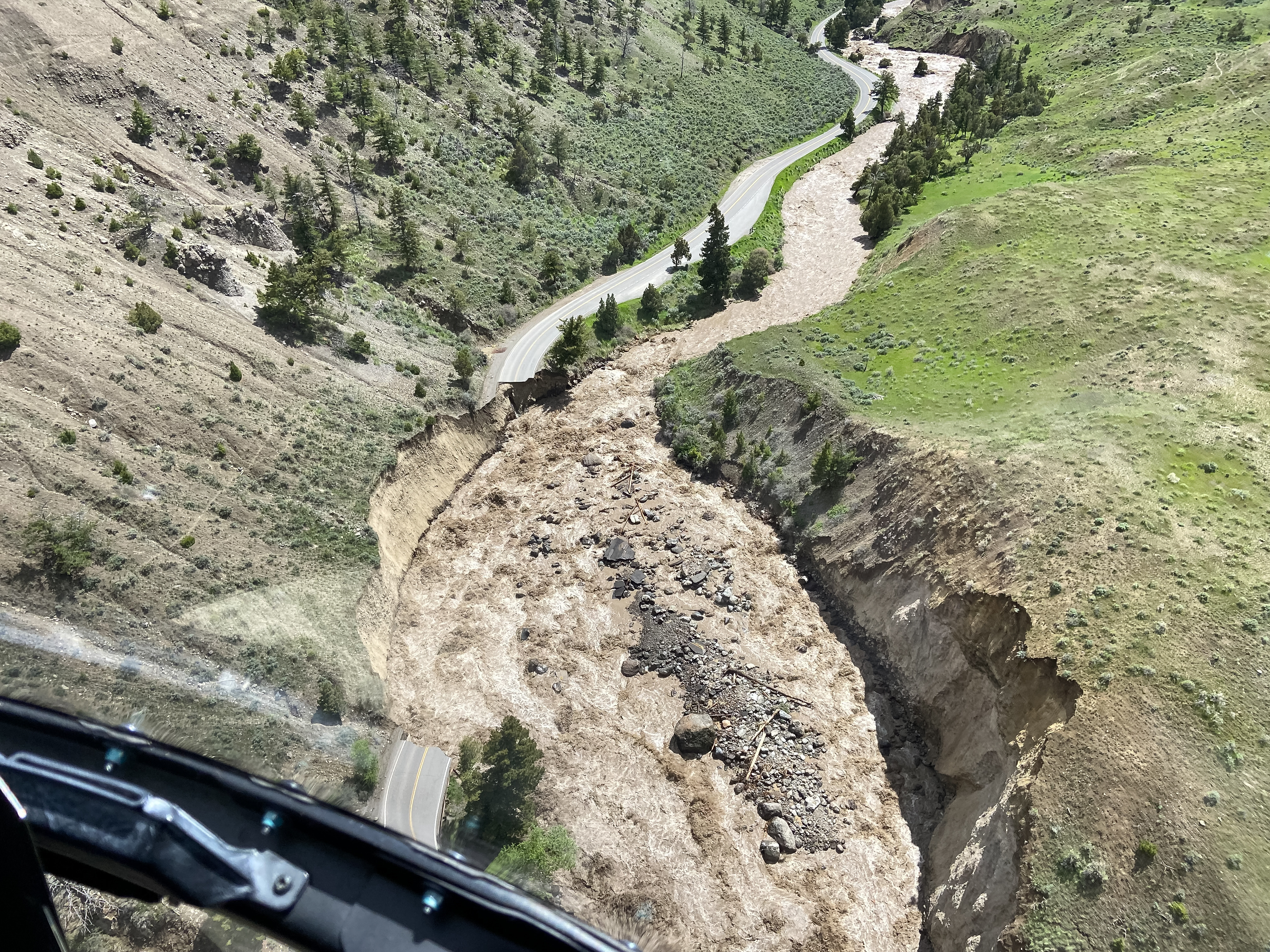 an aerial view of a washed-out and eroded paved road next to a river
