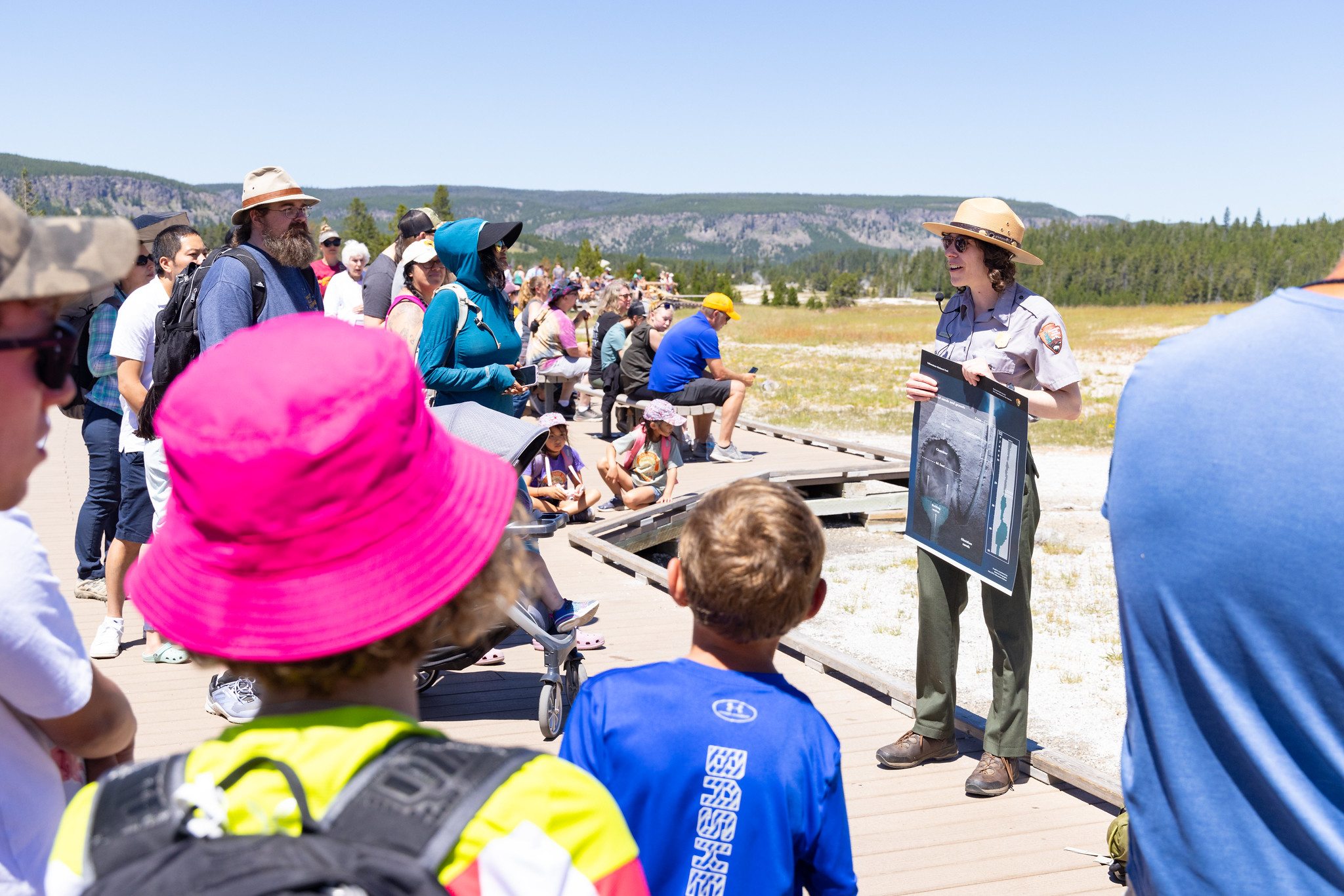 a park ranger giving an interpretive talk on a boardwalk near a thermal feature