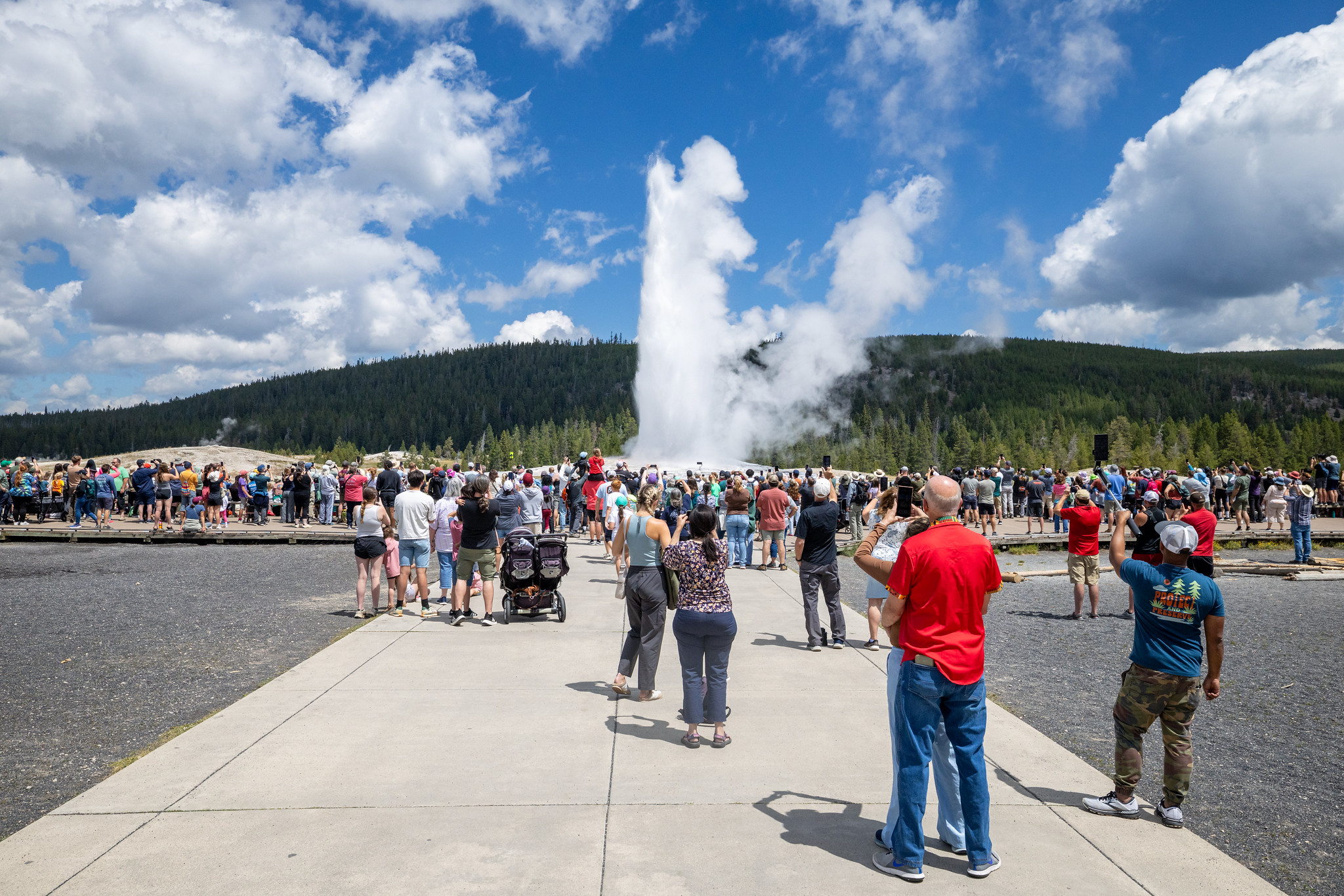 People watch an afternoon Old Faithful eruption