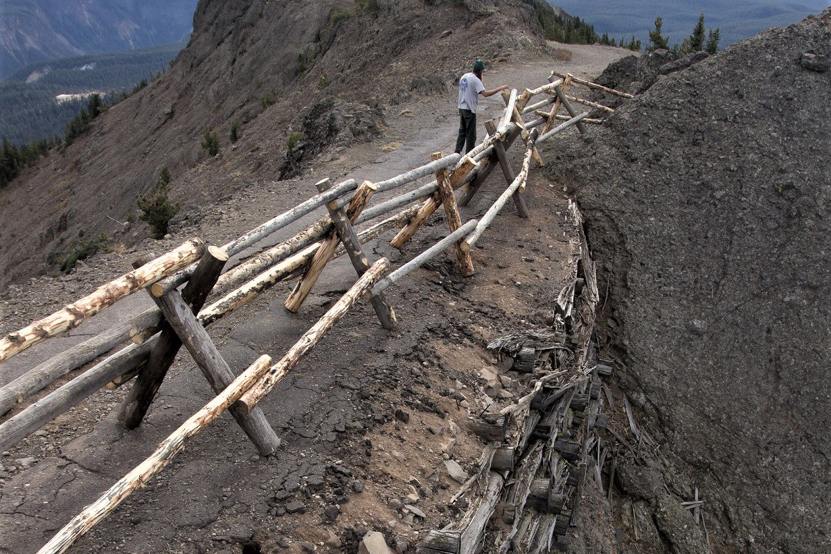 A person walks along a wooden fence with a rotten crib wall beneath the fence