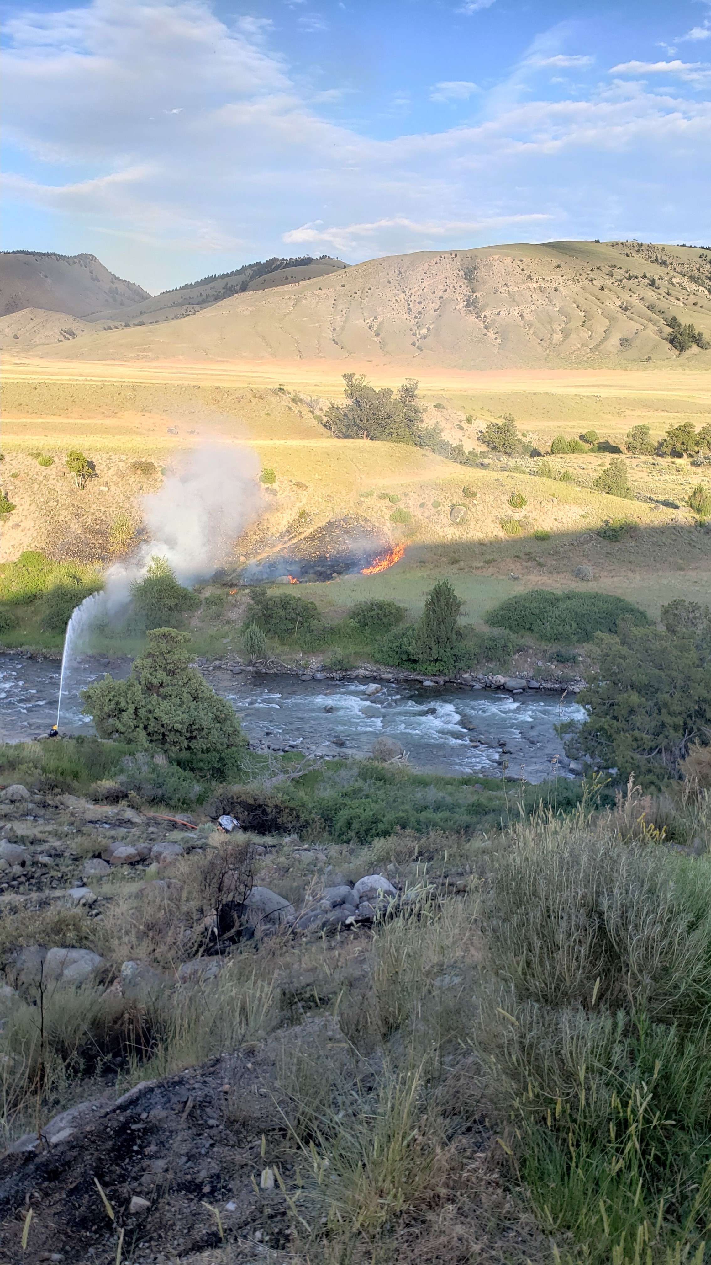 Wildire burning across a river and firefighter shooting hose of water at it