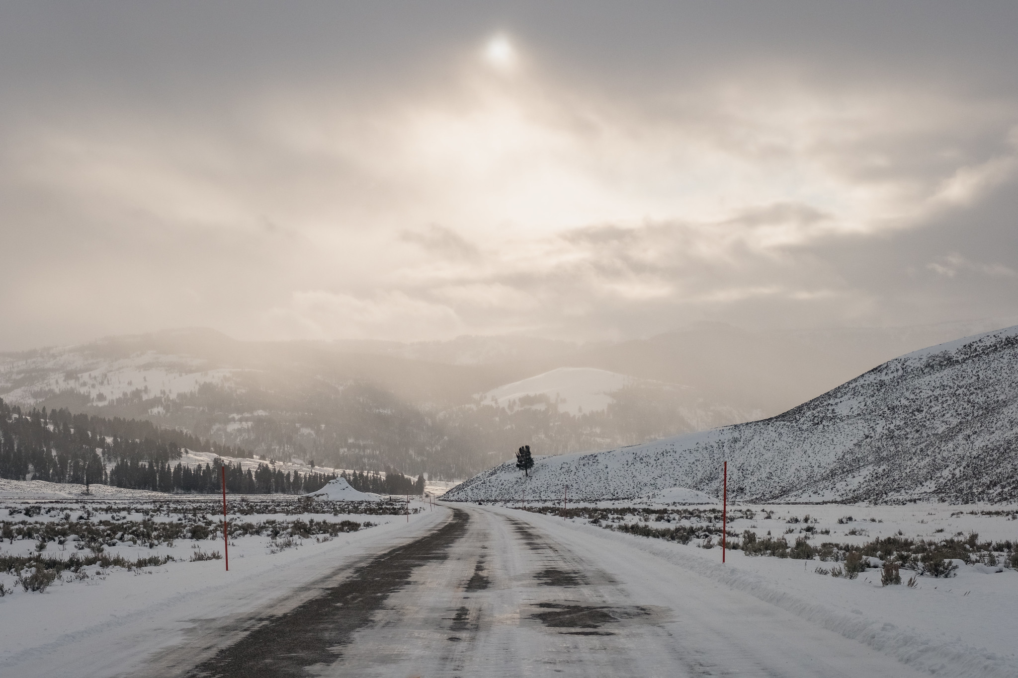 A snow- and ice-covered road in a mountainous landscape. Sunlight filters through the clouds.