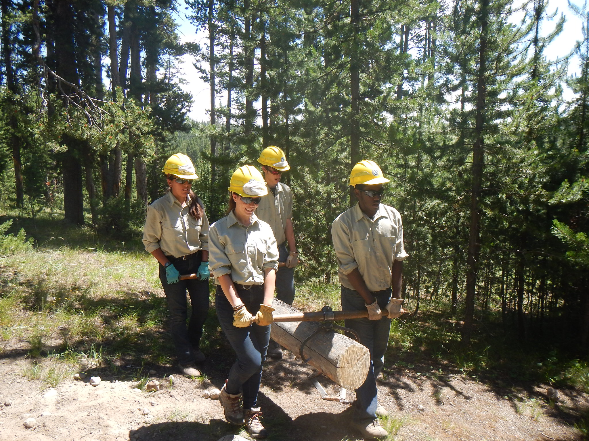 conservation corps members carrying a log