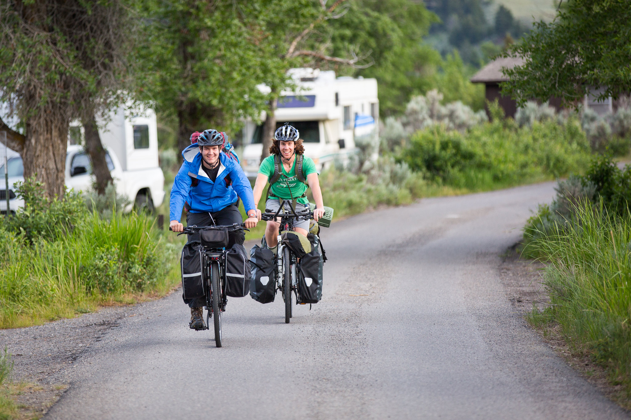 two smiling bicyclists riding on a paved road in a campground