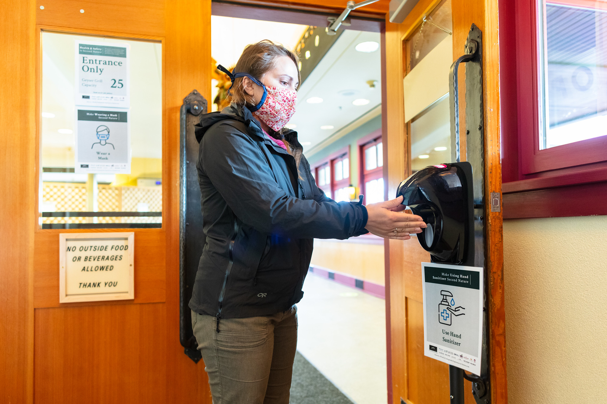 Mask wearing woman using hand sanitizer at the door to a restaurant