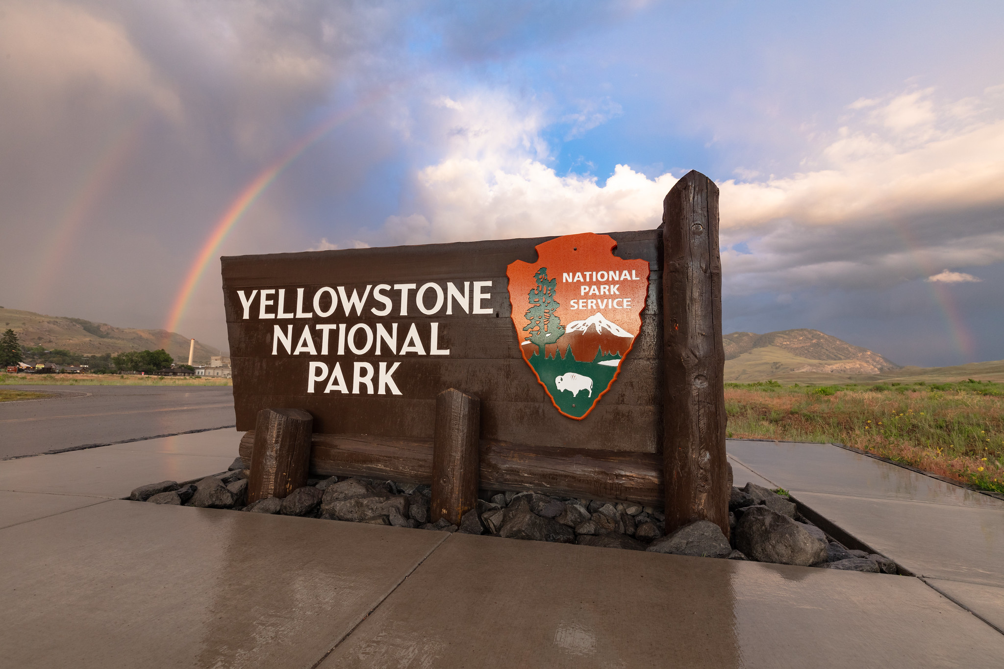 sign that reads "Yellowstone National Park" under a double rainbow
