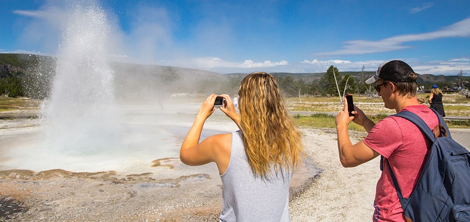 Two people photograph an erupting geyser