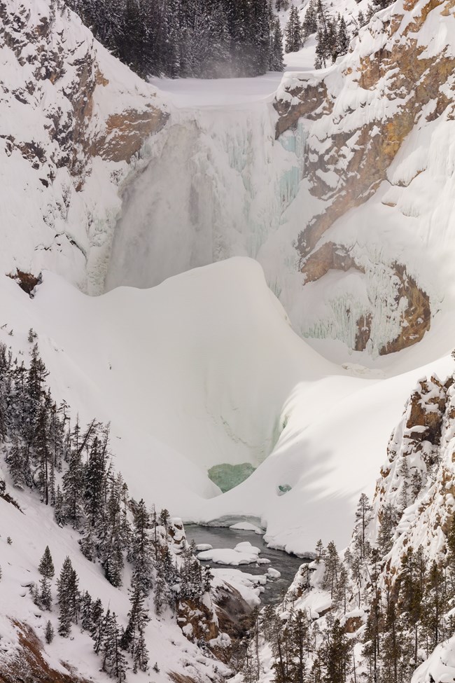 A large amount of snow and ice are built up around a large waterfall.