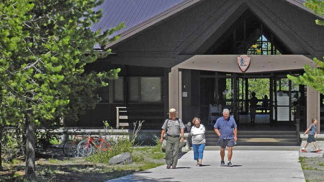 A ranger walks with a couple of visitors along a concrete path in front of the visitor center.