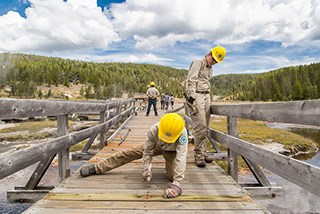 Two people in yellow hard hats work on a boardwalk.