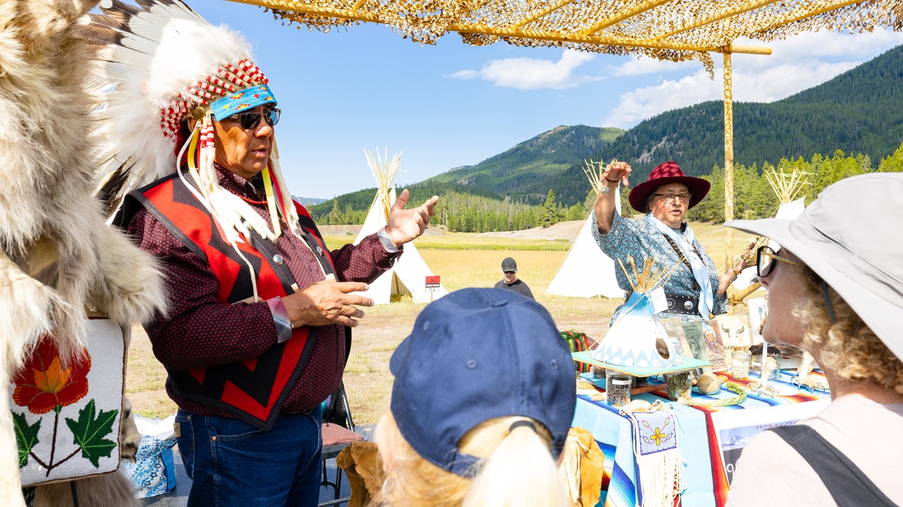 a man wearing a Native American headdress speaking to a group of people