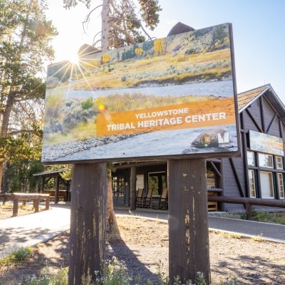 a large sign in front of a log cabin building that reads: "Yellowstone Tribal Heritage Center"