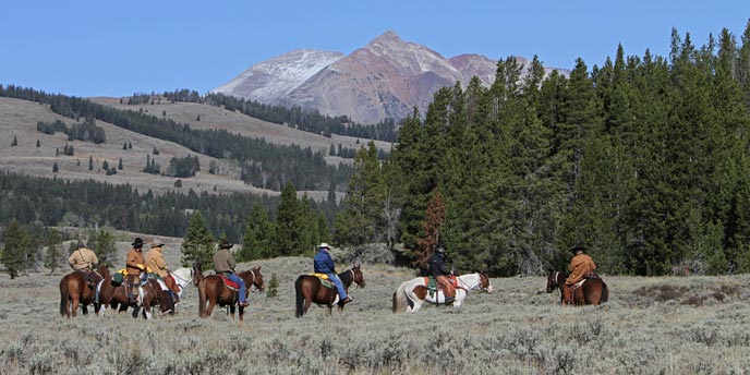 A group of riders on horseback stopped in the middle of sagebrush with a mountains in the background A group of riders on horseback stopped in the middle of sagebrush with a mountains in the background
