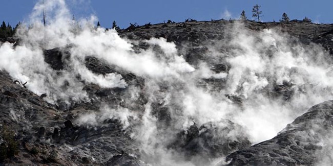 Steam rises from dark black rocks